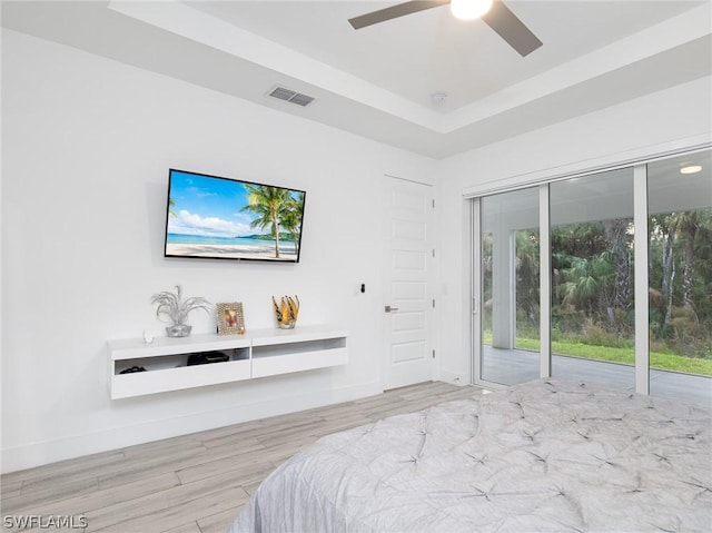 bedroom with light wood-type flooring, access to outside, a raised ceiling, and ceiling fan