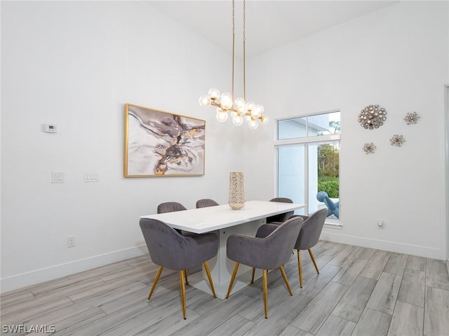 dining room featuring a chandelier, a towering ceiling, and light hardwood / wood-style floors