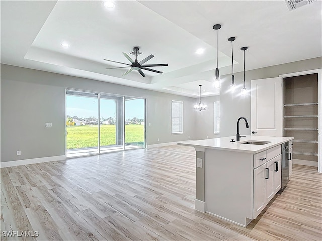 kitchen featuring light hardwood / wood-style floors, an island with sink, ceiling fan with notable chandelier, a raised ceiling, and sink