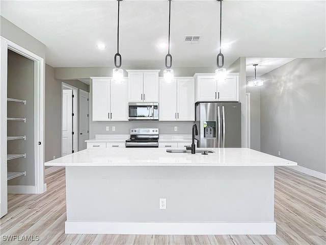 kitchen with a center island with sink, appliances with stainless steel finishes, decorative light fixtures, and sink