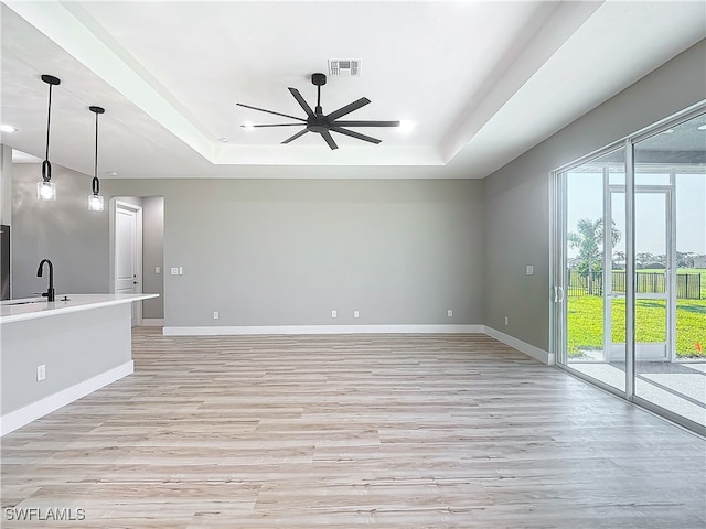 unfurnished living room with a raised ceiling, ceiling fan, light hardwood / wood-style flooring, and sink