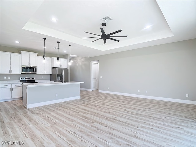 kitchen with appliances with stainless steel finishes, a raised ceiling, a center island with sink, and ceiling fan