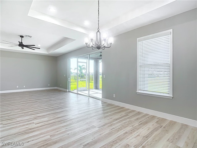 spare room with ceiling fan with notable chandelier, a tray ceiling, and light hardwood / wood-style flooring