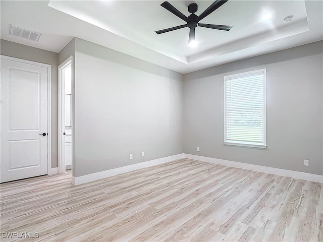 unfurnished room featuring light hardwood / wood-style flooring, ceiling fan, and a raised ceiling