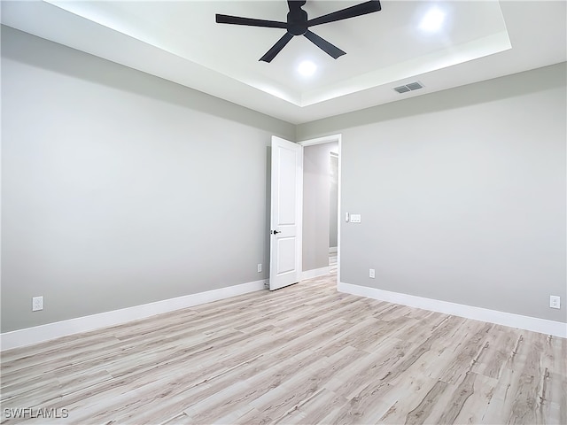 empty room featuring light wood-type flooring, a raised ceiling, and ceiling fan