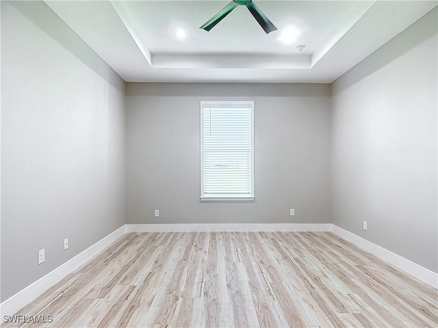 empty room featuring ceiling fan, light hardwood / wood-style flooring, and a tray ceiling