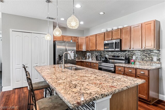 kitchen featuring stainless steel appliances, dark wood-type flooring, hanging light fixtures, sink, and a kitchen island with sink