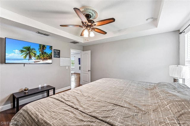 bedroom featuring dark wood-type flooring, ceiling fan, and a tray ceiling