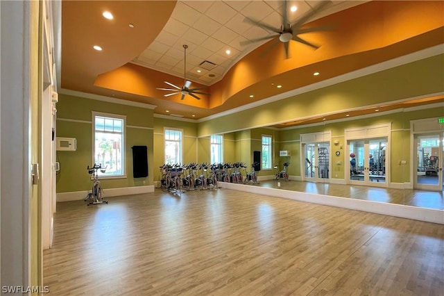 workout area featuring french doors, a towering ceiling, a raised ceiling, ceiling fan, and wood-type flooring