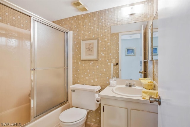 full bathroom with toilet, vanity, tile walls, and bath / shower combo with glass door