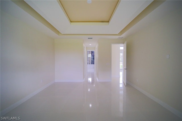 hallway with tile patterned flooring and a tray ceiling