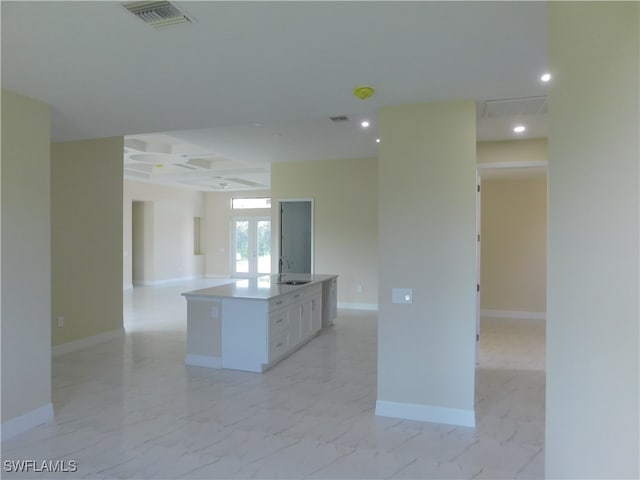 kitchen with white cabinets, sink, a center island, coffered ceiling, and light tile patterned floors