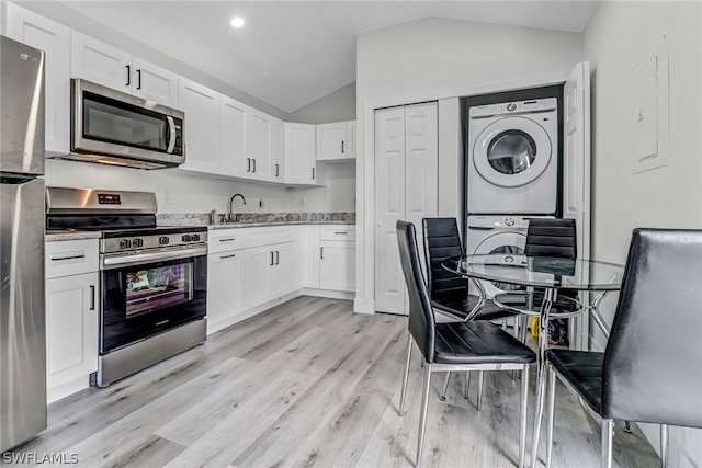 kitchen with lofted ceiling, light hardwood / wood-style flooring, appliances with stainless steel finishes, stacked washer / drying machine, and white cabinetry