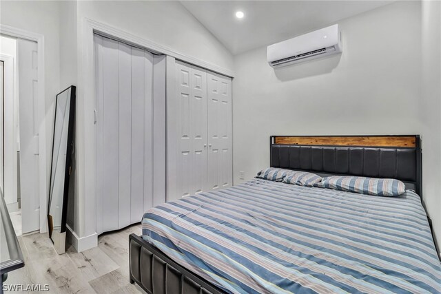 bedroom featuring vaulted ceiling, light hardwood / wood-style floors, a wall unit AC, and a closet