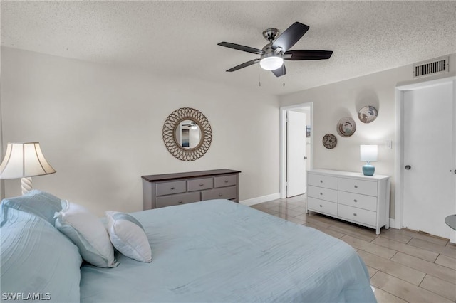 bedroom featuring light tile patterned floors, a ceiling fan, baseboards, visible vents, and a textured ceiling