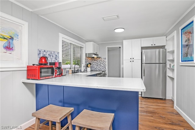 kitchen with appliances with stainless steel finishes, kitchen peninsula, white cabinets, and hardwood / wood-style floors