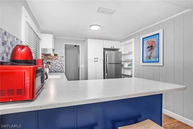 kitchen featuring light hardwood / wood-style flooring, kitchen peninsula, white cabinets, backsplash, and stainless steel fridge