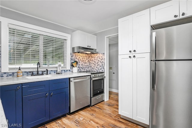 kitchen with white cabinetry, blue cabinets, stainless steel appliances, light wood-type flooring, and backsplash