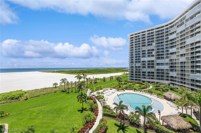 view of swimming pool featuring a water view, a view of the beach, and a lawn