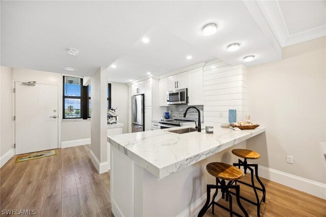 kitchen featuring kitchen peninsula, a kitchen breakfast bar, light wood-type flooring, white cabinets, and appliances with stainless steel finishes