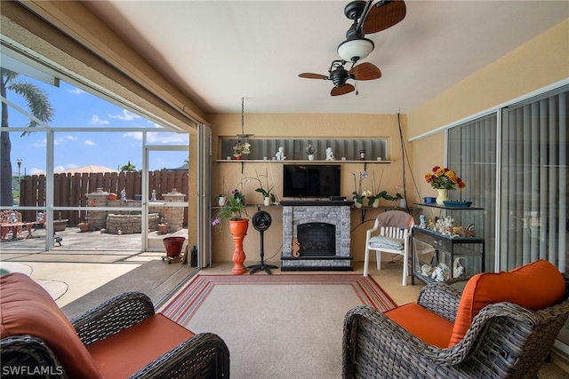 sunroom with ceiling fan and a stone fireplace