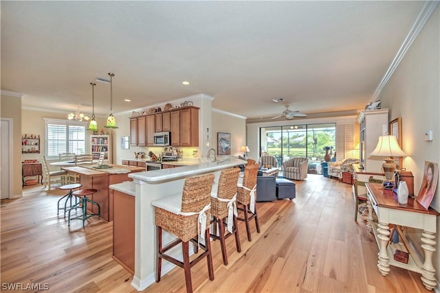 kitchen featuring kitchen peninsula, a kitchen bar, ceiling fan with notable chandelier, stainless steel appliances, and hanging light fixtures