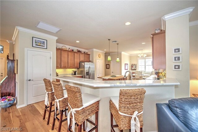 kitchen featuring kitchen peninsula, stainless steel fridge, pendant lighting, a kitchen bar, and light wood-type flooring