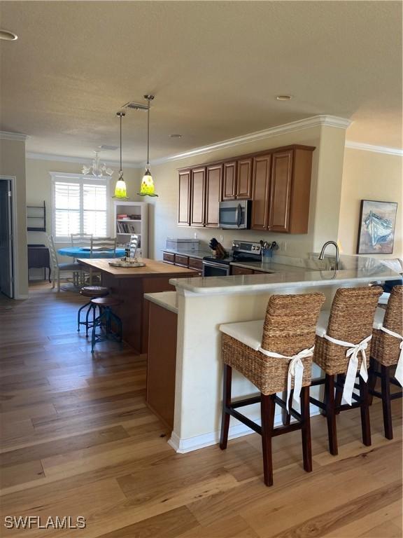 kitchen with stainless steel appliances, kitchen peninsula, light hardwood / wood-style floors, decorative light fixtures, and a breakfast bar