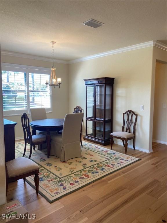 dining space with hardwood / wood-style floors, crown molding, and an inviting chandelier