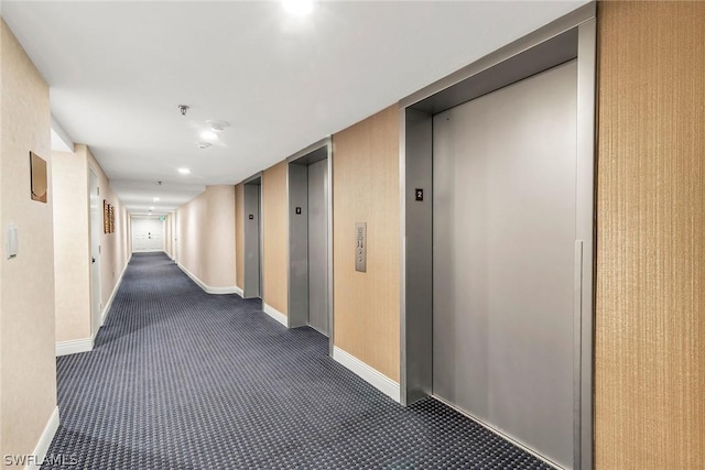 hallway with elevator and dark colored carpet