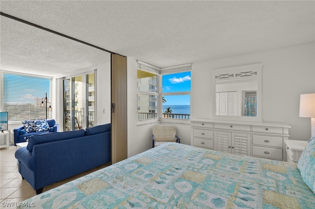 bedroom featuring a textured ceiling, floor to ceiling windows, a water view, and light tile patterned floors