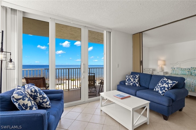 living room featuring floor to ceiling windows, a water view, a textured ceiling, and light tile patterned floors