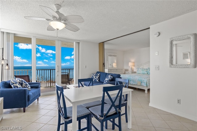 tiled dining area with floor to ceiling windows, a textured ceiling, ceiling fan, and a water view