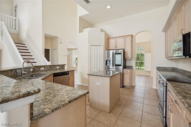 kitchen with appliances with stainless steel finishes, a center island, a towering ceiling, dark stone counters, and sink