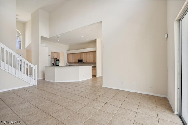 unfurnished living room with sink, light tile patterned floors, and a towering ceiling