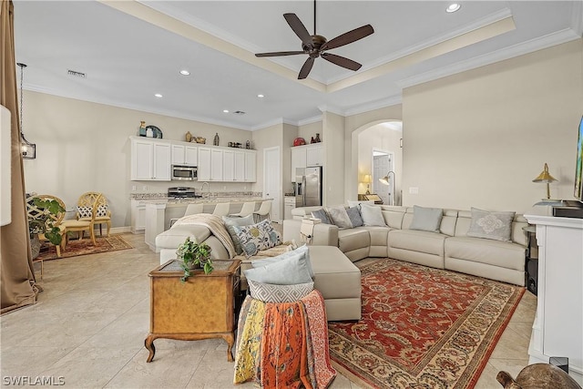 living room with ceiling fan, a raised ceiling, sink, and crown molding