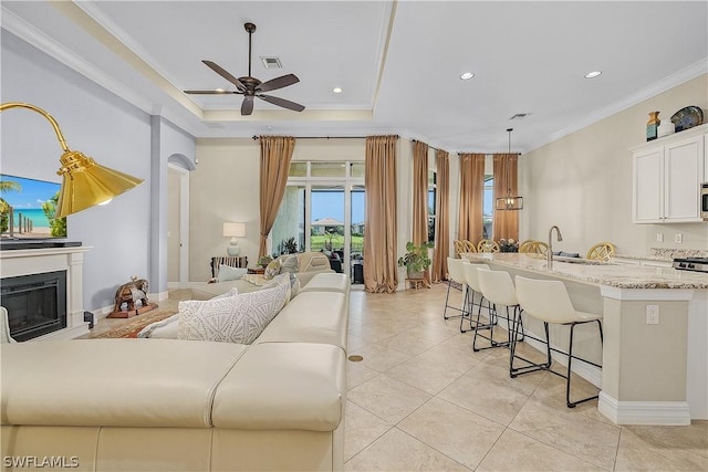 tiled living room with a raised ceiling, ceiling fan, sink, and ornamental molding