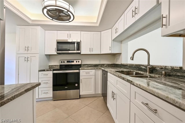 kitchen featuring white cabinetry, stainless steel appliances, dark stone counters, and a tray ceiling