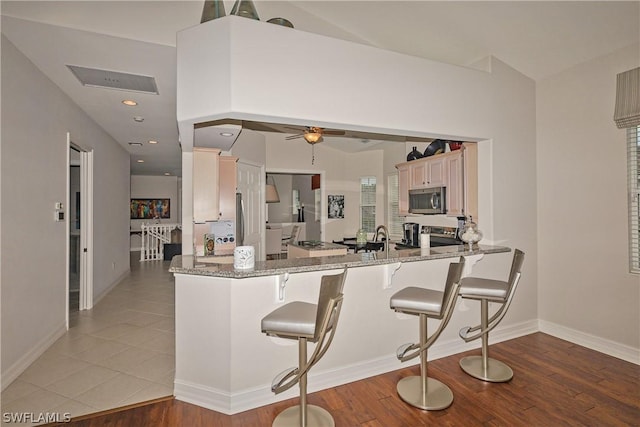 kitchen featuring tile patterned flooring, ceiling fan, kitchen peninsula, and stone counters