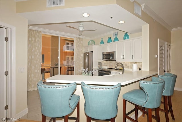 kitchen featuring white cabinets, decorative backsplash, ceiling fan, ornamental molding, and appliances with stainless steel finishes