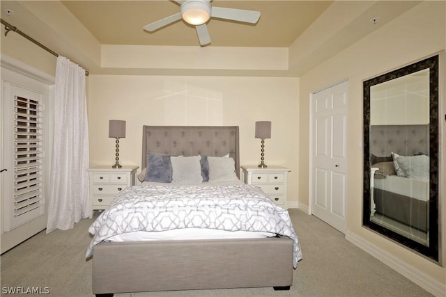 bedroom with a raised ceiling, ceiling fan, and light colored carpet