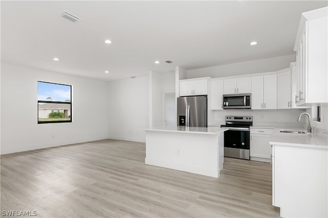 kitchen with stainless steel appliances, white cabinets, sink, a kitchen island, and light wood-type flooring