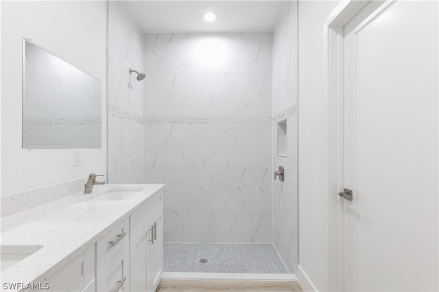 bathroom with a tile shower, hardwood / wood-style flooring, and dual bowl vanity