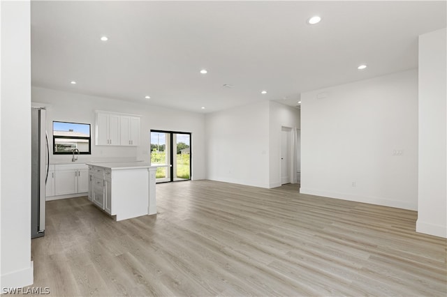 interior space with white cabinets, stainless steel fridge, sink, light wood-type flooring, and a center island