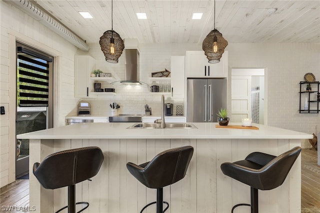 kitchen featuring a large island with sink, high end refrigerator, hanging light fixtures, and wall chimney exhaust hood