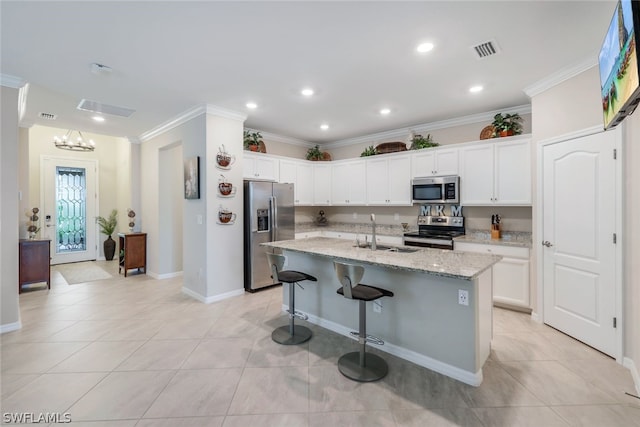 kitchen with sink, white cabinetry, stainless steel appliances, light stone countertops, and an island with sink