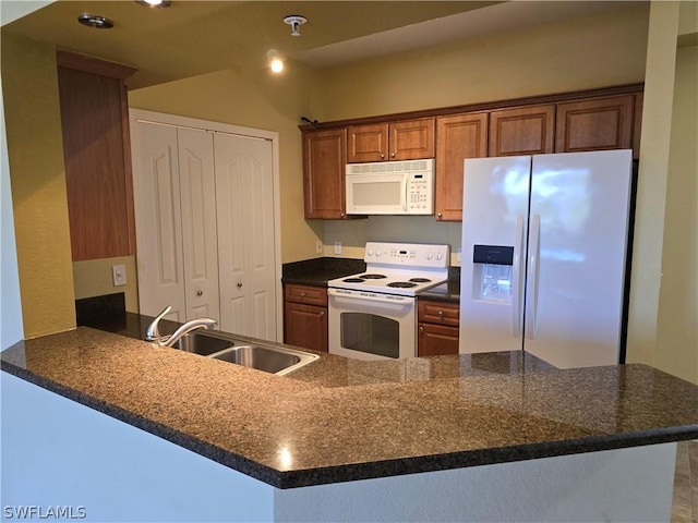 kitchen featuring white appliances, brown cabinetry, a peninsula, a sink, and dark countertops