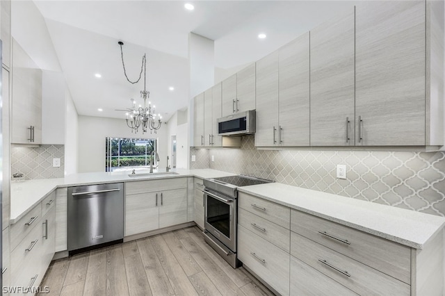 kitchen featuring stainless steel appliances, sink, light hardwood / wood-style flooring, kitchen peninsula, and a notable chandelier