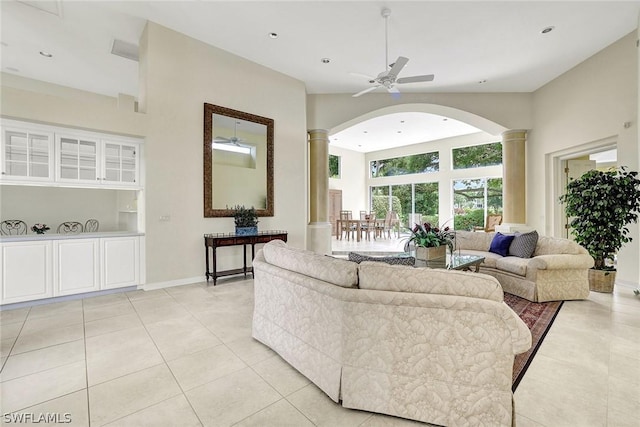 tiled living room featuring ceiling fan, a high ceiling, and decorative columns