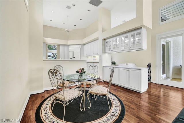 dining area with ceiling fan, a towering ceiling, and dark wood-type flooring